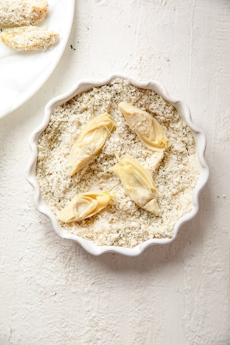 dredging artichoke hearts in a parmesan breadcrumb mix