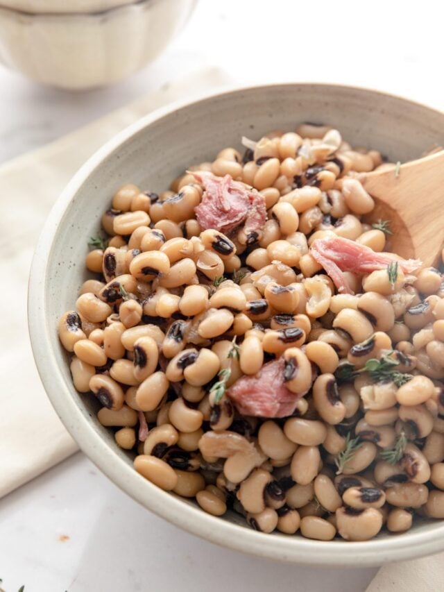 A close-up of Instant Pot black eyed peas in a bowl with ham and a wooden spoon.