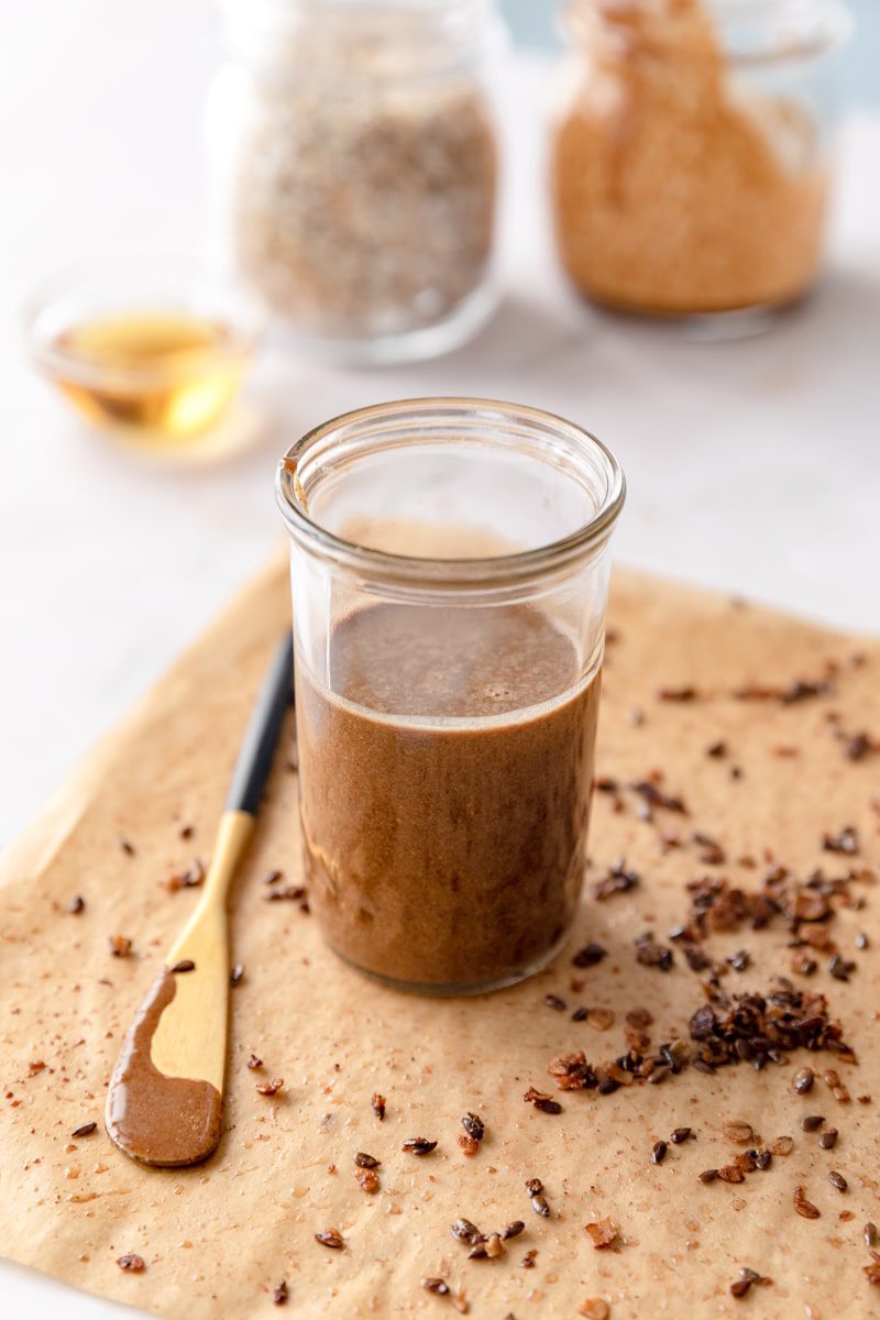 glass mason jar of granola butter sitting on a piece of parchment paper