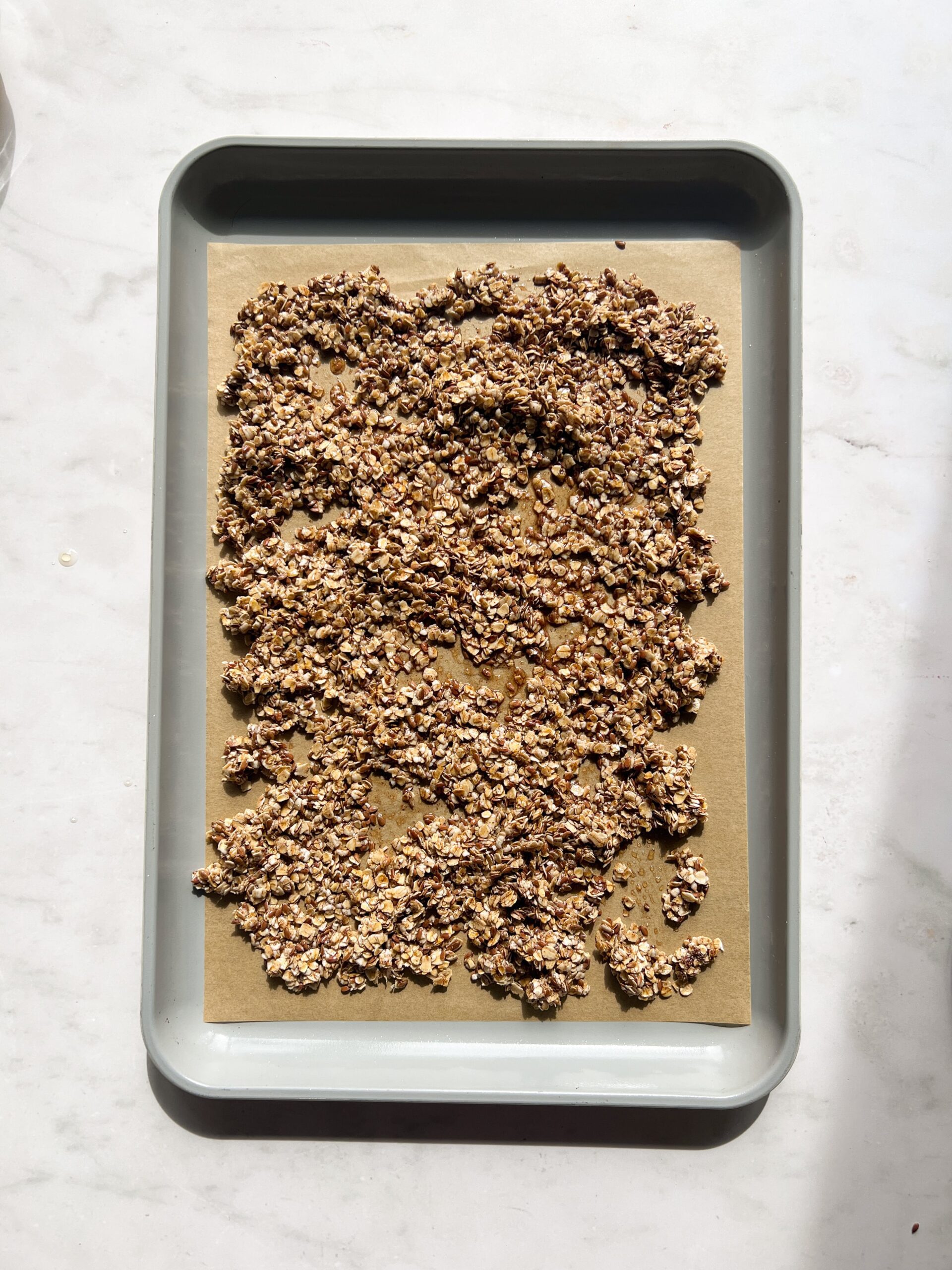 granola spread on a baking sheet before being toasted