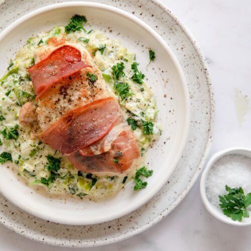 overhead photo of prosciutto wrapped chicken on a white plate