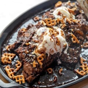 close up photo of brownie in a skillet with ice cream, caramel, and pretzel toppings