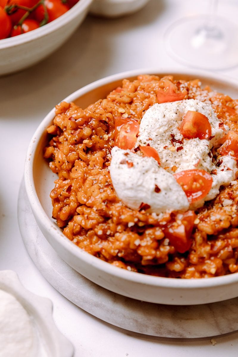 close up photo of a bowl of tomato risotto with a ball of burrata cheese on top