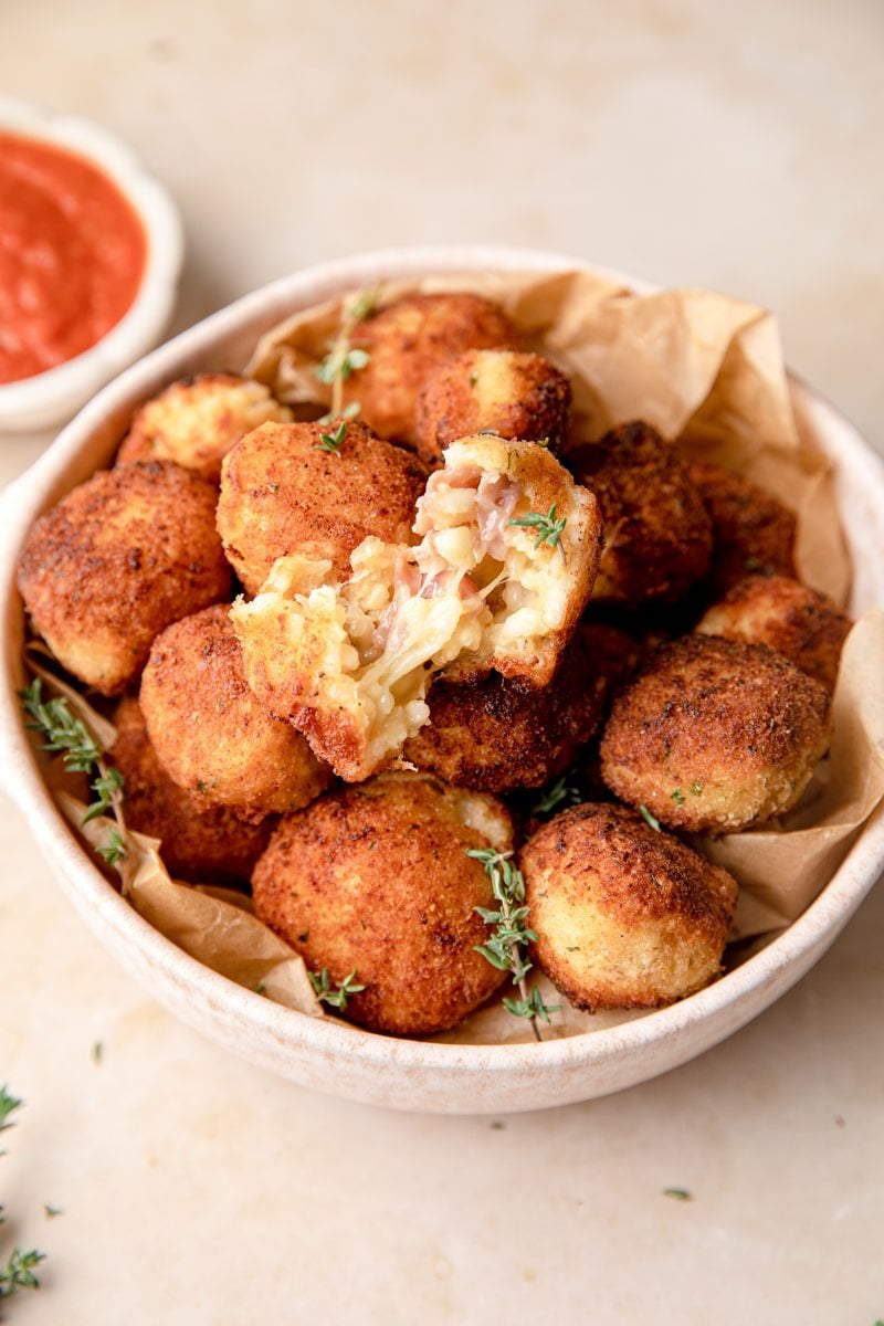 bowl of arancini with one torn in half exposing the rice and cheese