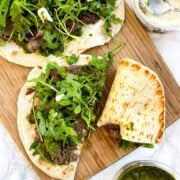 An overhead shot of steak chimichurri flatbreads on a cutting board.