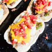 An overhead angled shot of flaming hot cheesesteaks on the blackstone.