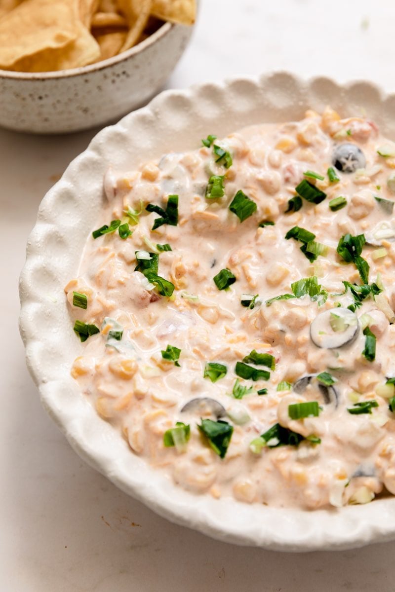 cream cheese corn dip served up in a white scalloped bowl with tortilla chips on the side