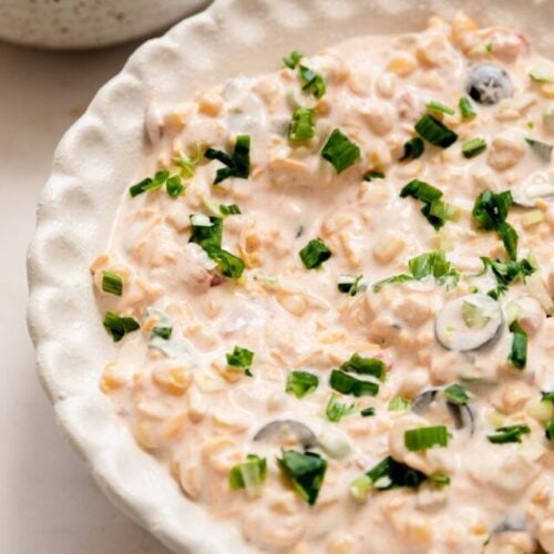 cream cheese corn dip served up in a white scalloped bowl with tortilla chips on the side