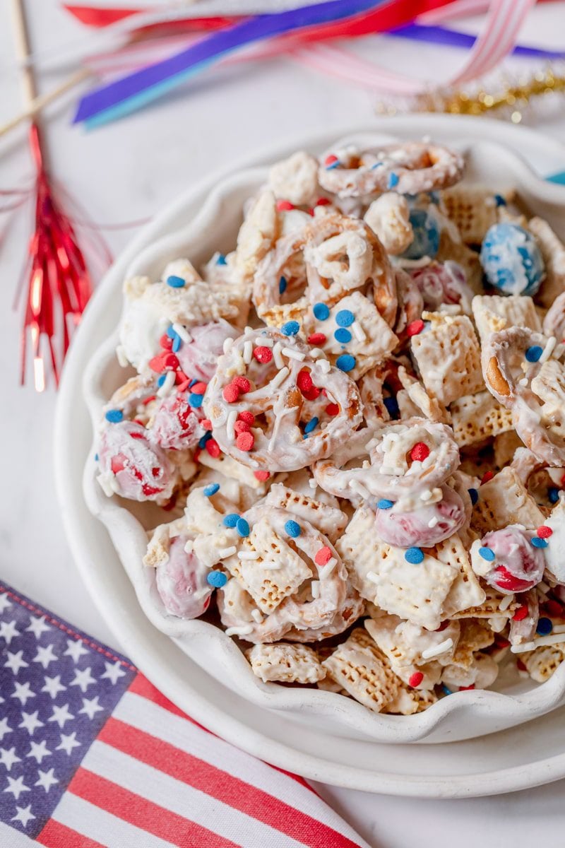 white bowl of patriotic party mix with American flags surrounding