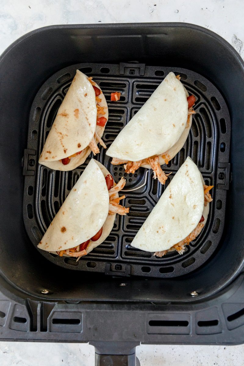filled street tacos folded in half in an air fryer basket 
