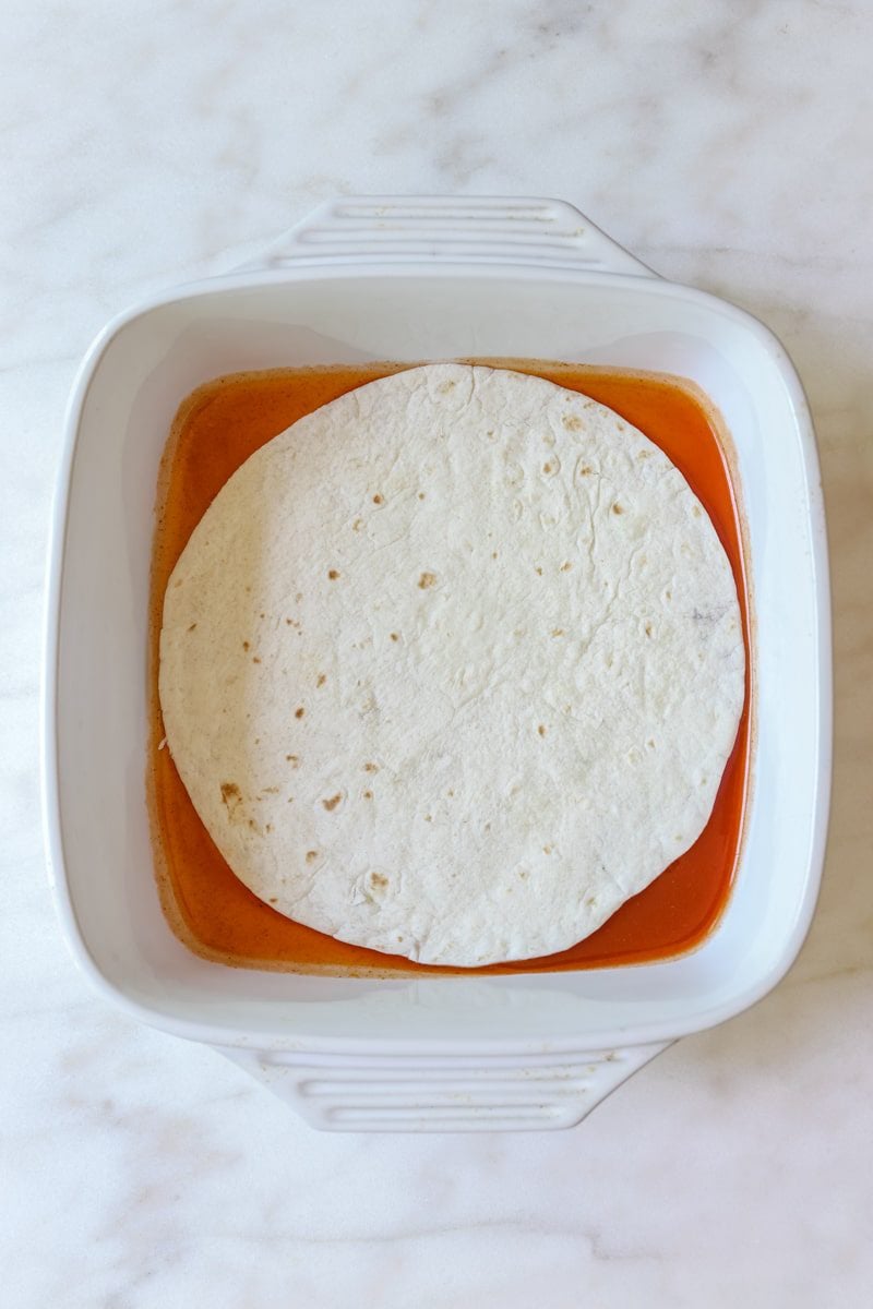 casserole dish with enchilada sauce and a flour tortilla