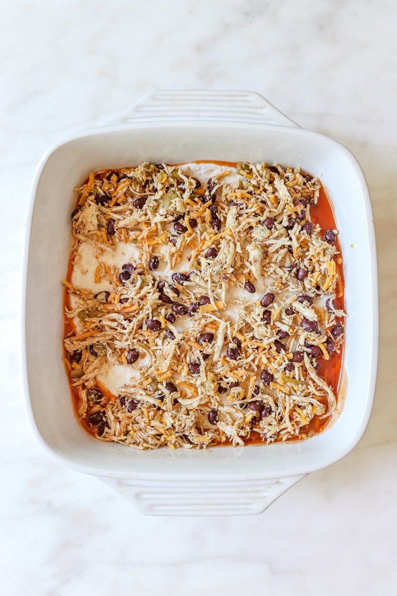 shredded chicken mixture on top of the tortilla and enchilada sauce layered in a casserole dish