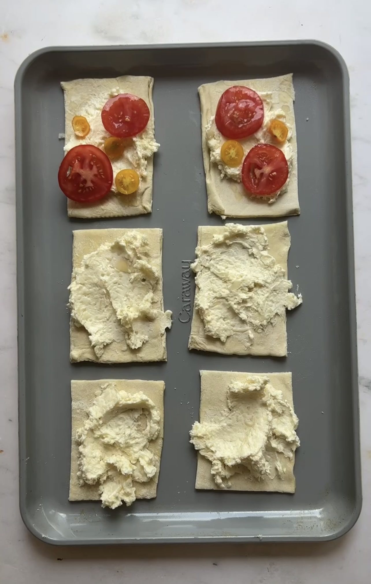 mini tomato puff pastry tarts on a sheet tray with cheese spread and tomatoes on top.