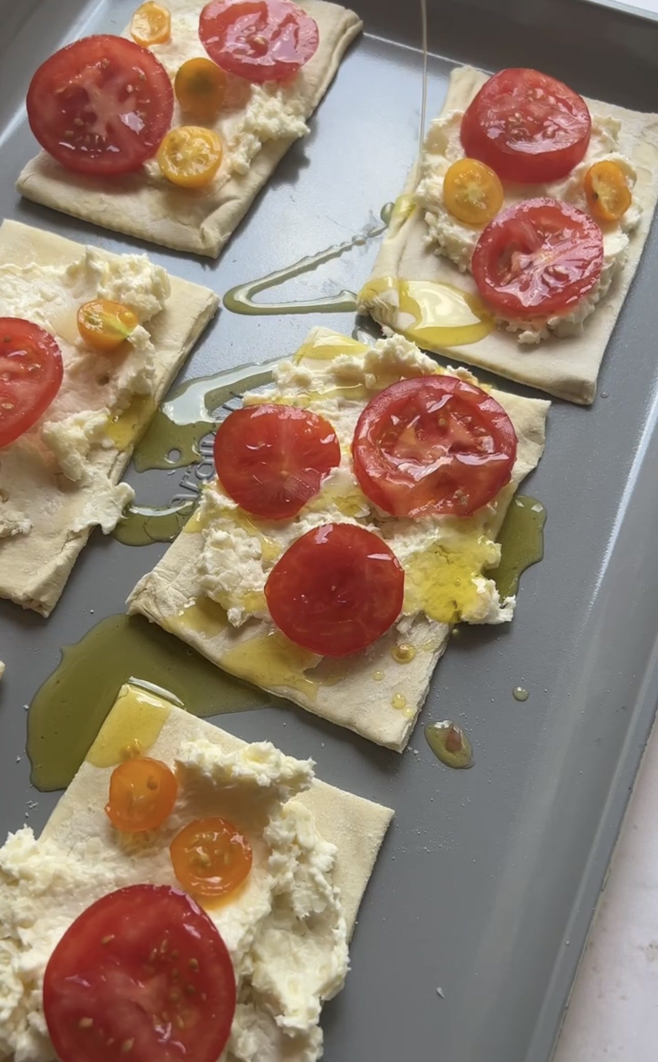 tomato tarts on a sheet tray topped with cheese, tomatoes, and olive oil.