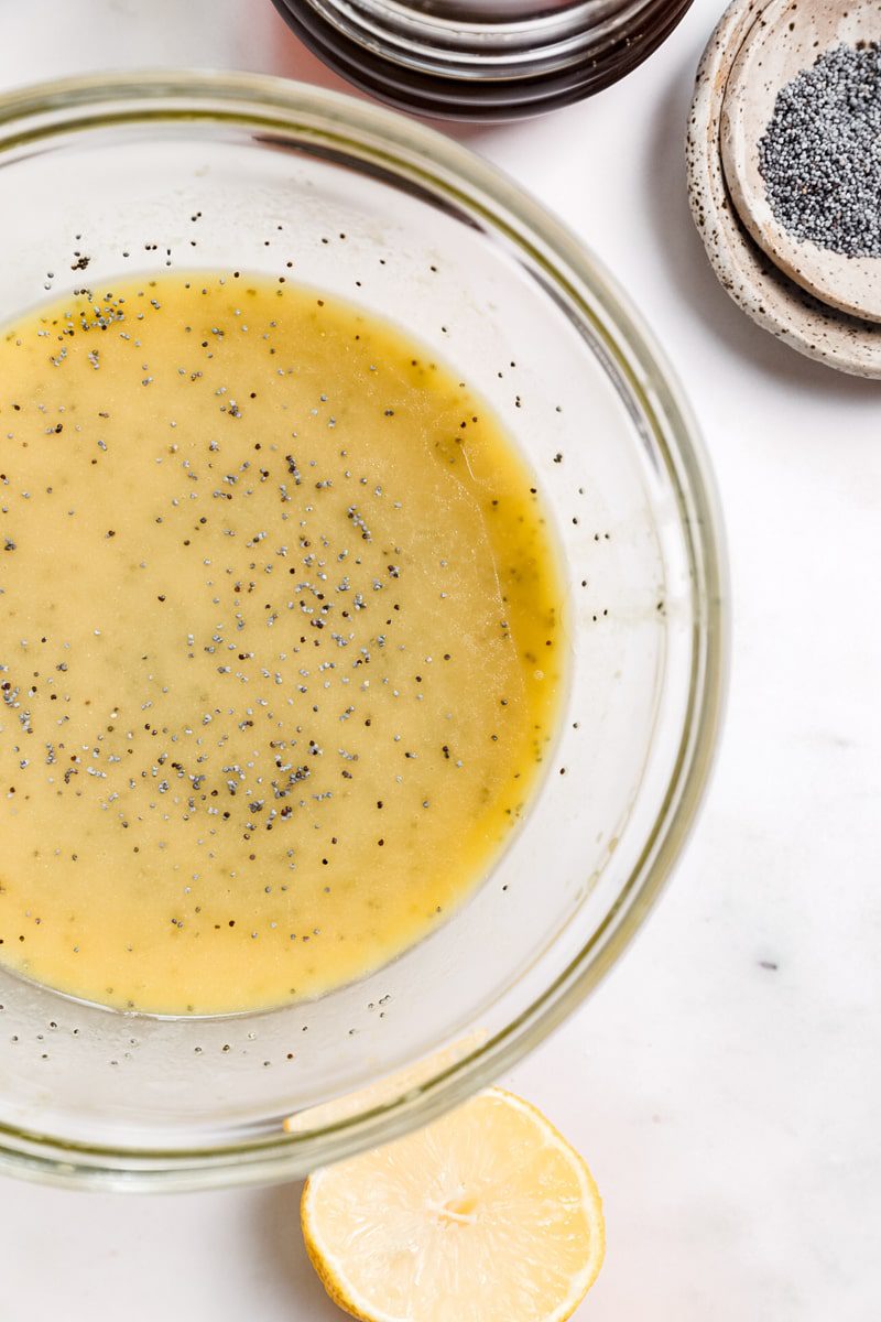 glass mixing bowl of mixed creamy, lemon poppy seed dressing