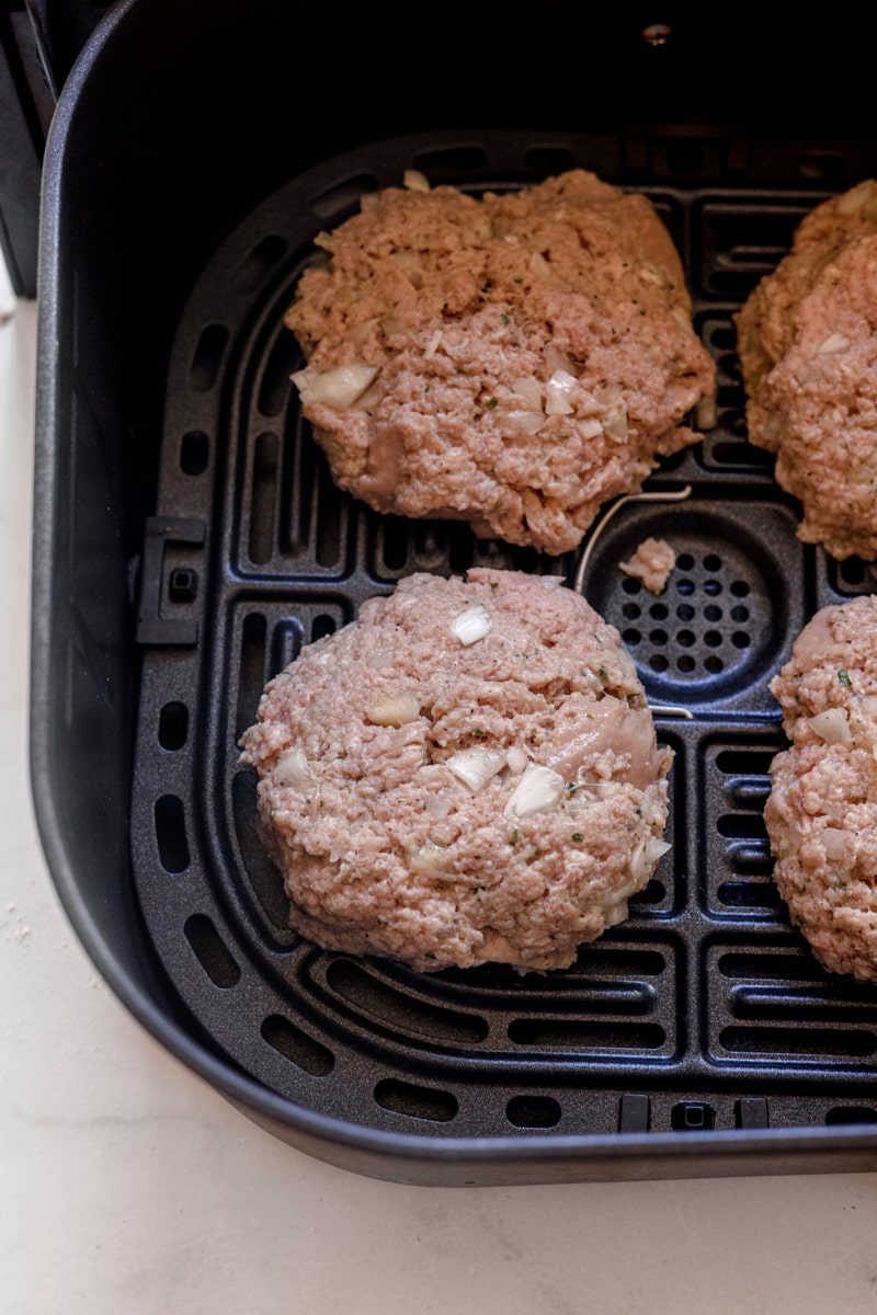 raw turkey burger patties in an air fryer basket 