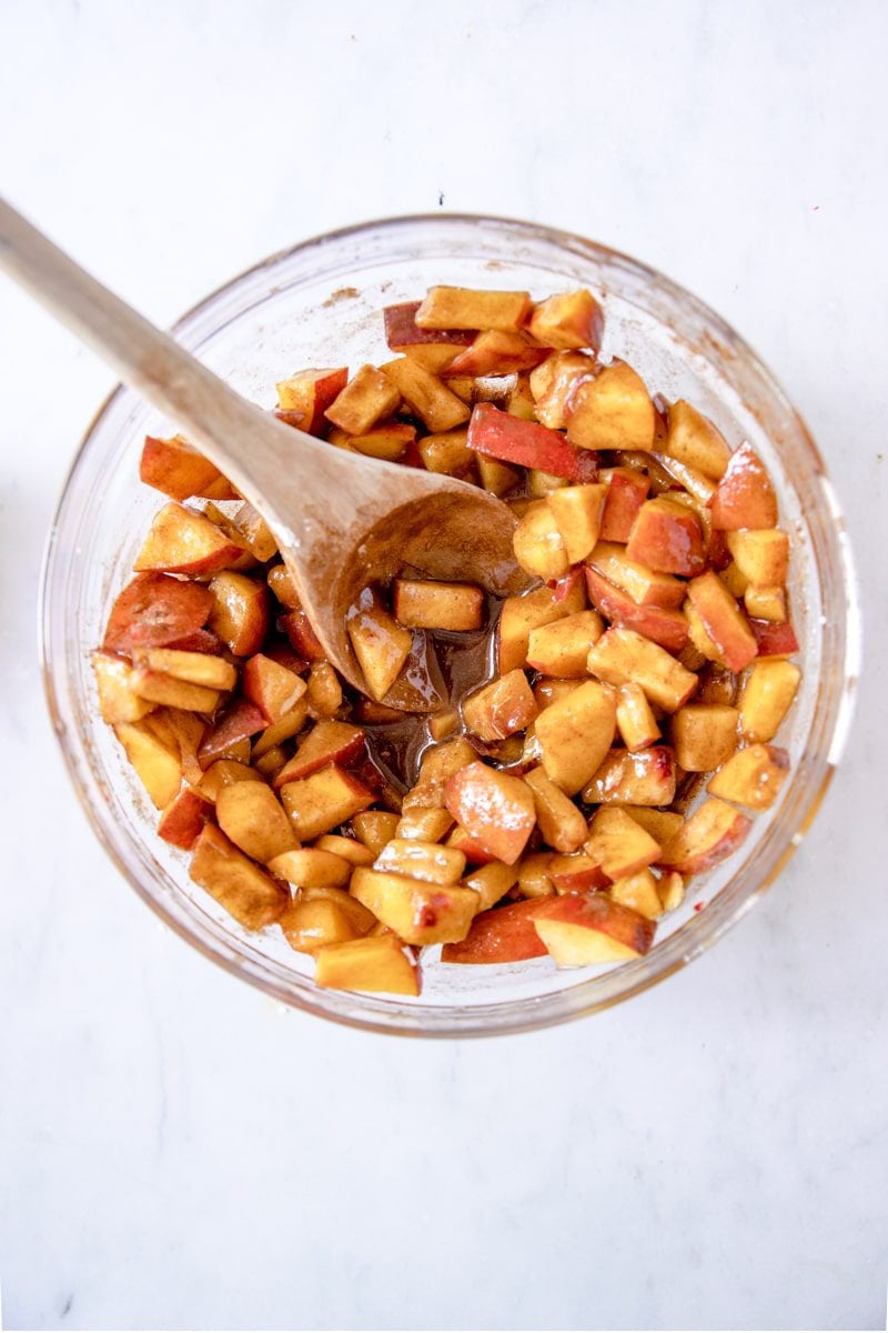 peaches, cinnamon, agave, cornstarch, and brown sugar mixed together in a glass mixing bowl