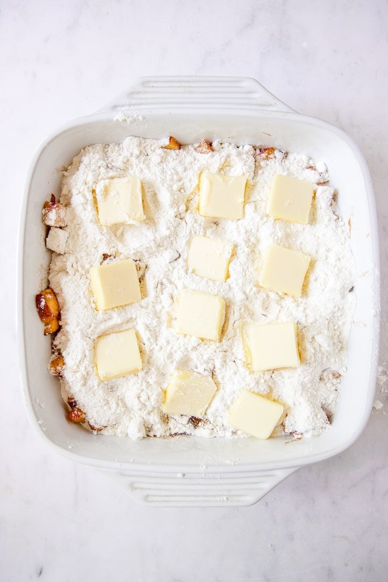 baking dish layered with peach filling, cake mix, and pats of butter ready for the oven