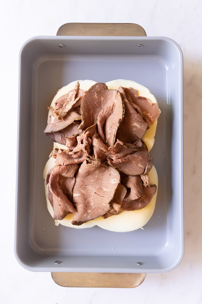 bottom half of slider buns in a baking dish layered with cheese and roast beef