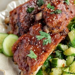 oven baked ribs on a white plate with a cucumber salad next to it.