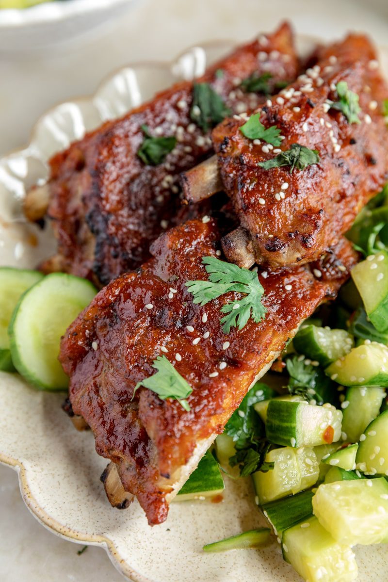oven baked ribs on a white plate with a cucumber salad next to it.