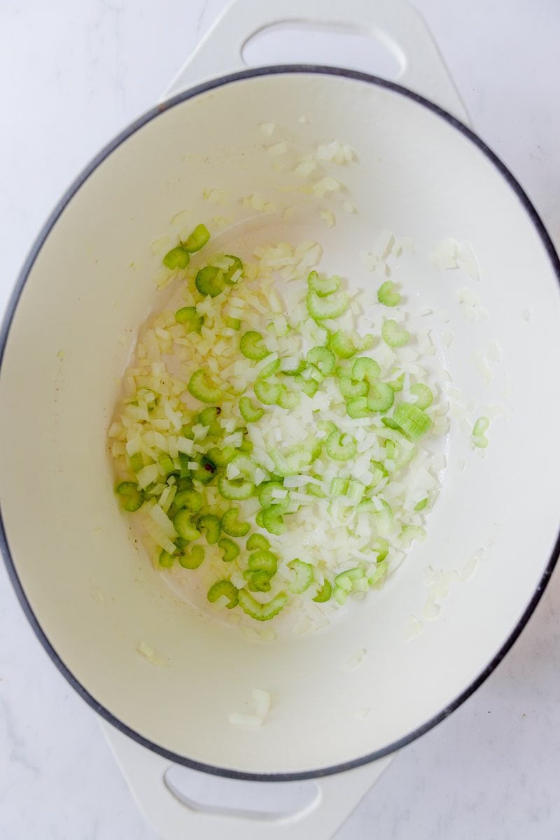 overhead photo of onion, garlic, and celery sautéed in a white dutch oven 