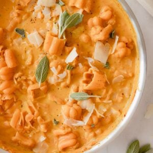 skillet of creamy pumpkin pasta sauce garnished with sage and black pepper