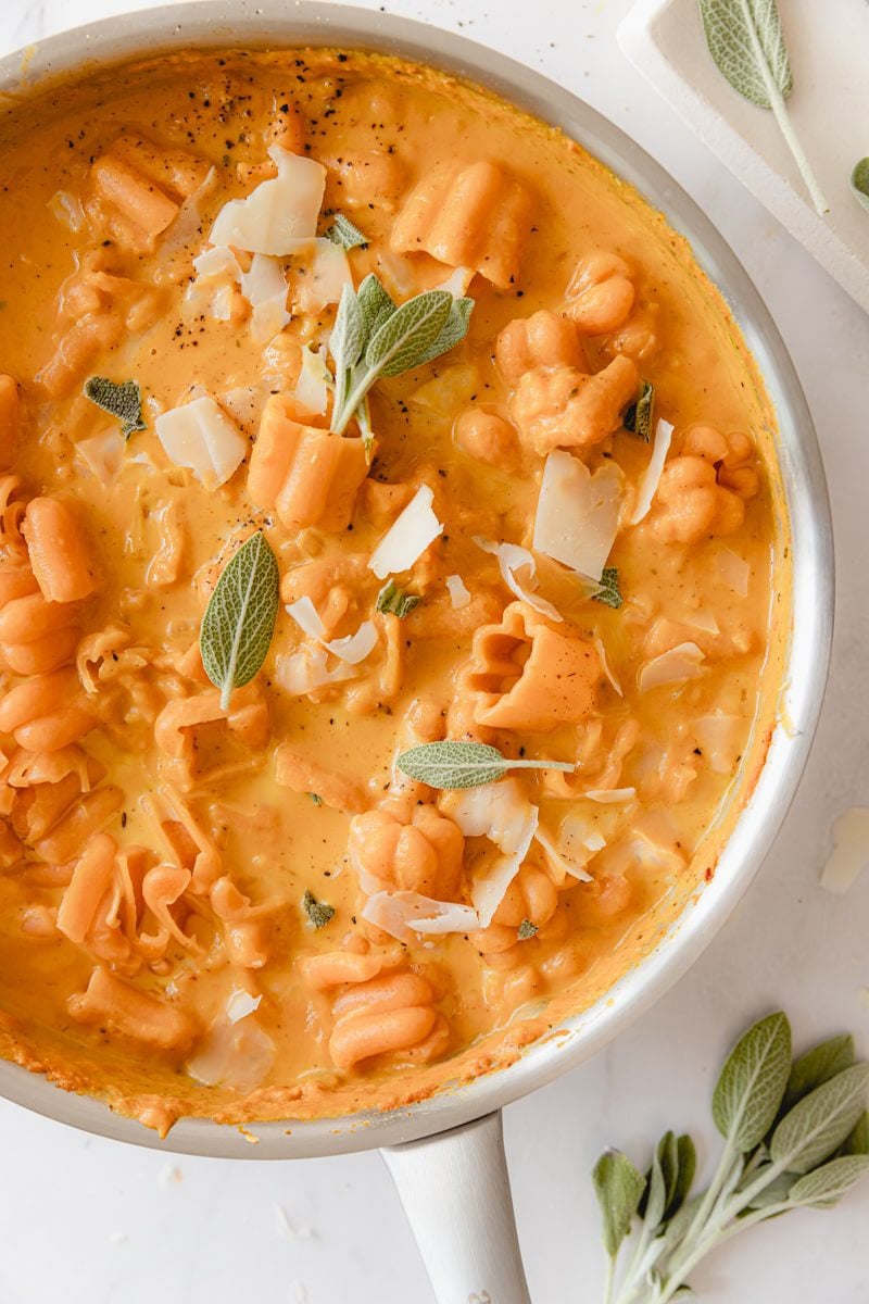 skillet of creamy pumpkin pasta sauce garnished with sage and black pepper