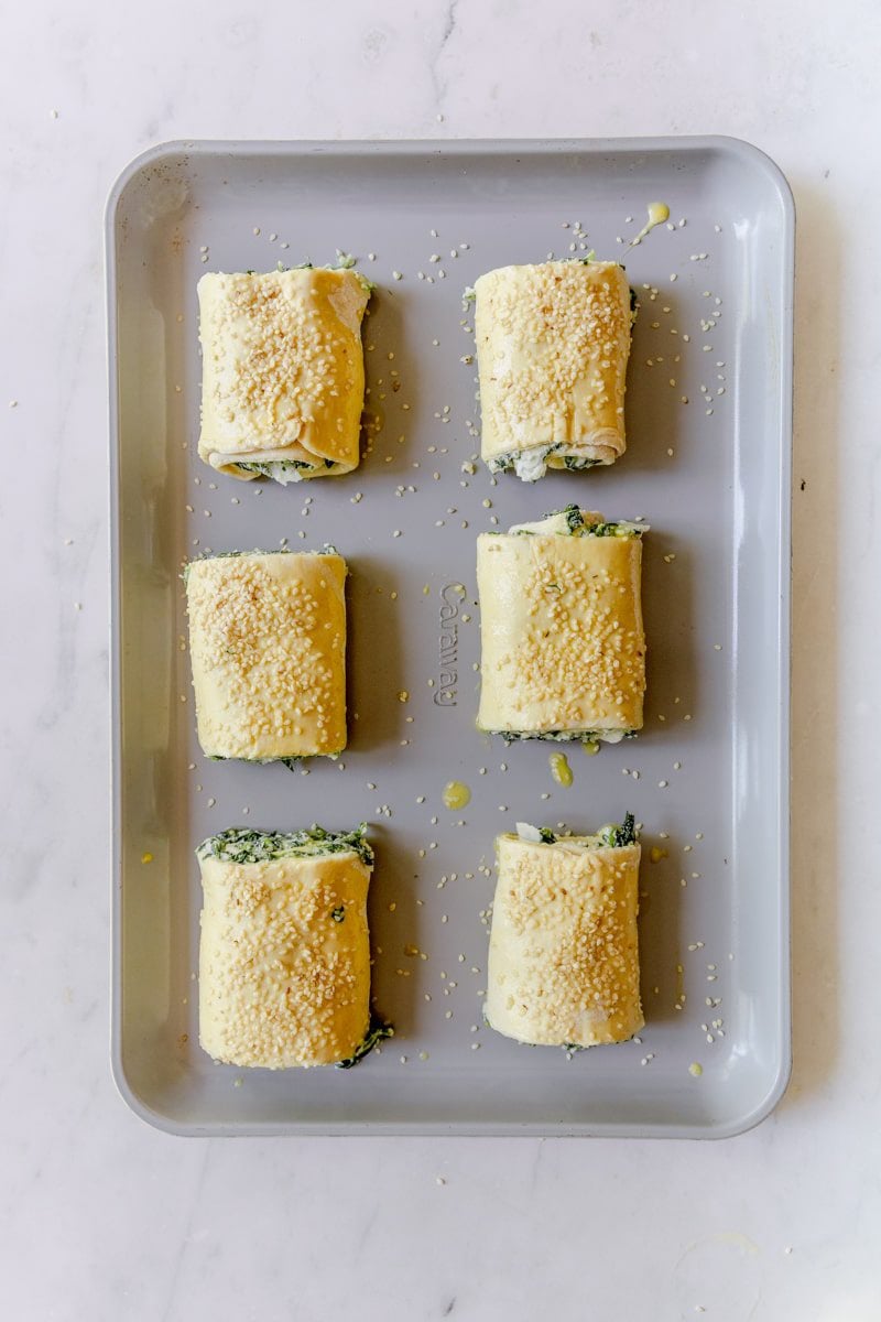 raw spinach and ricotta roll ups brushed with egg wash and sesame seeds on a baking sheet