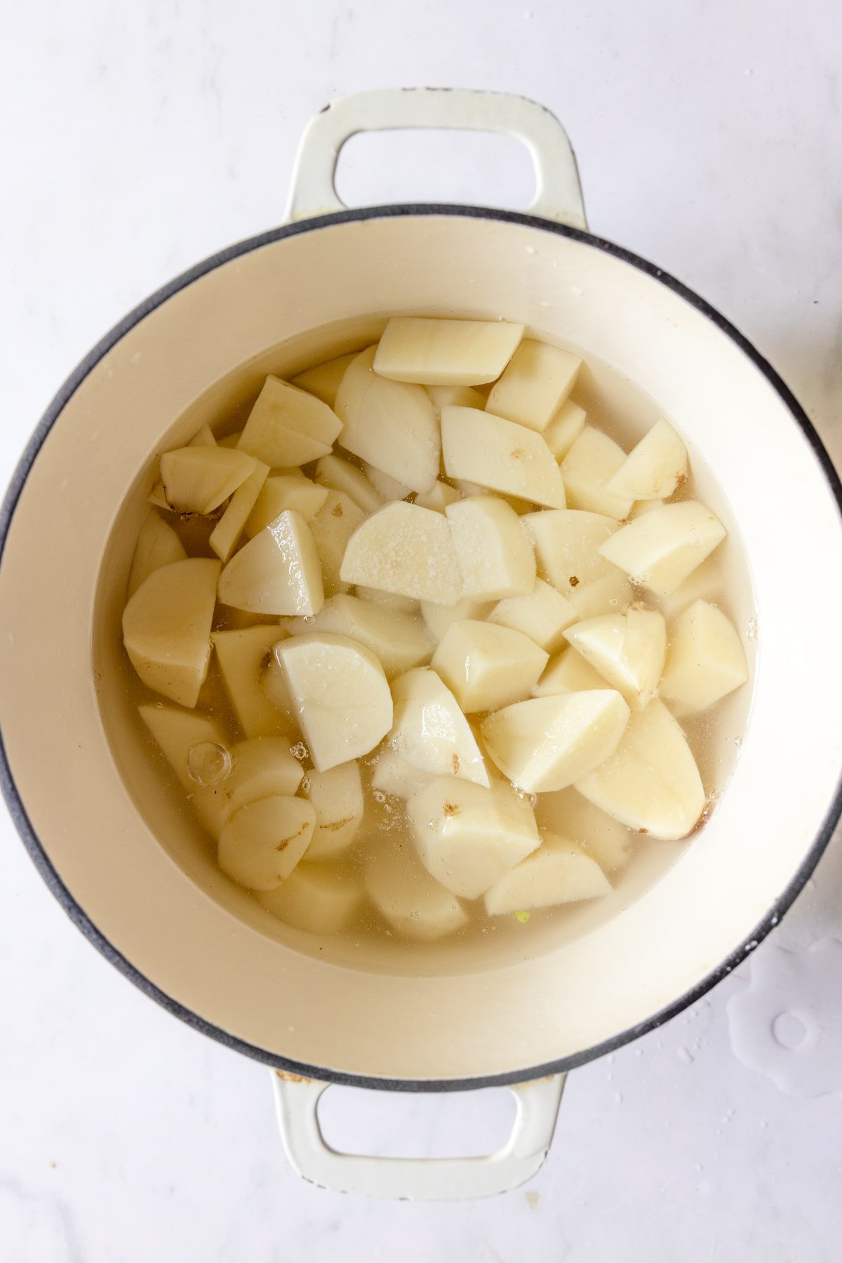 potatoes in a white dutch oven covered with water.