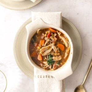 turkey lentil soup in a white bowl with a napkin and spoon laying next to it.
