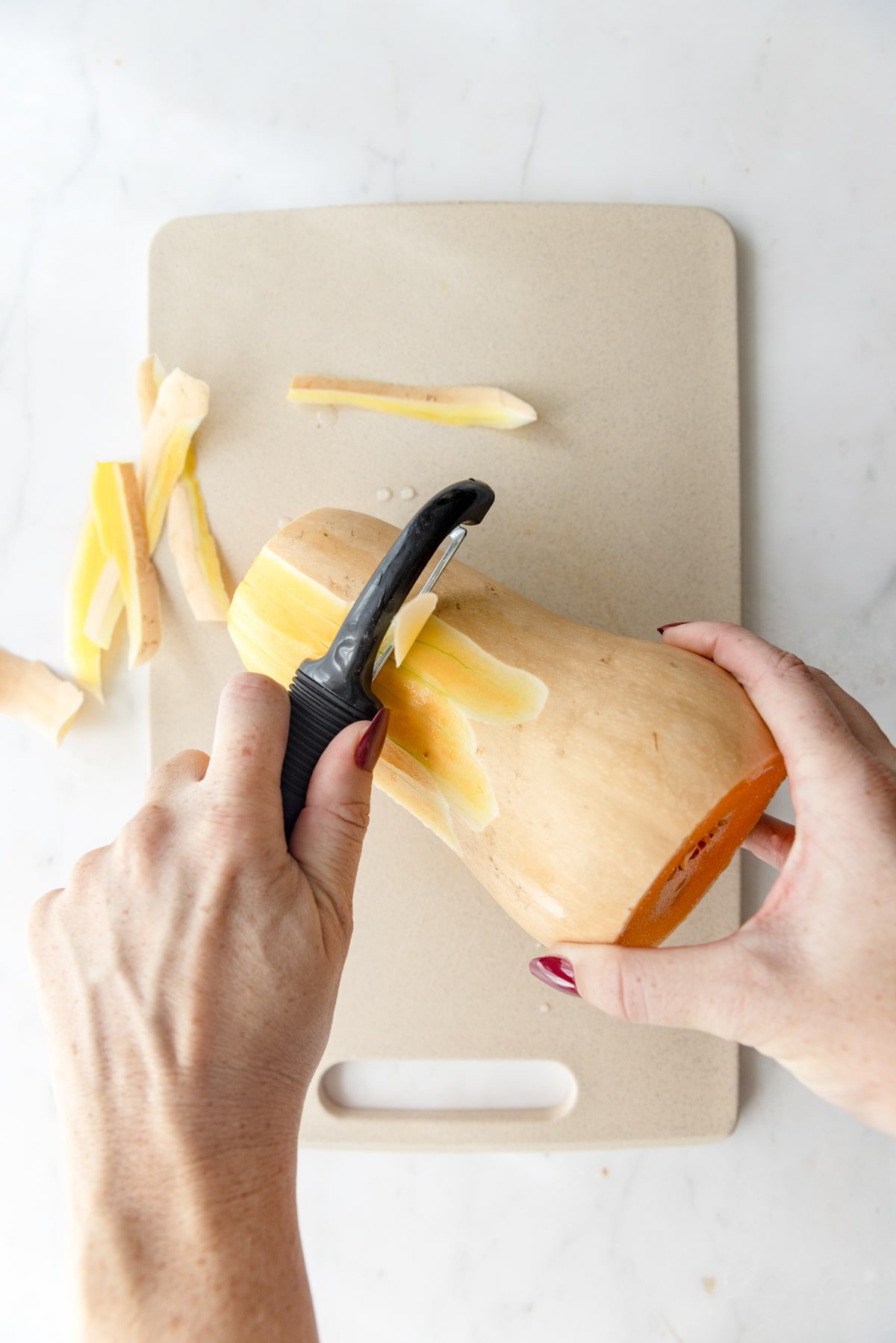 peeling a butternut squash on a cutting board.