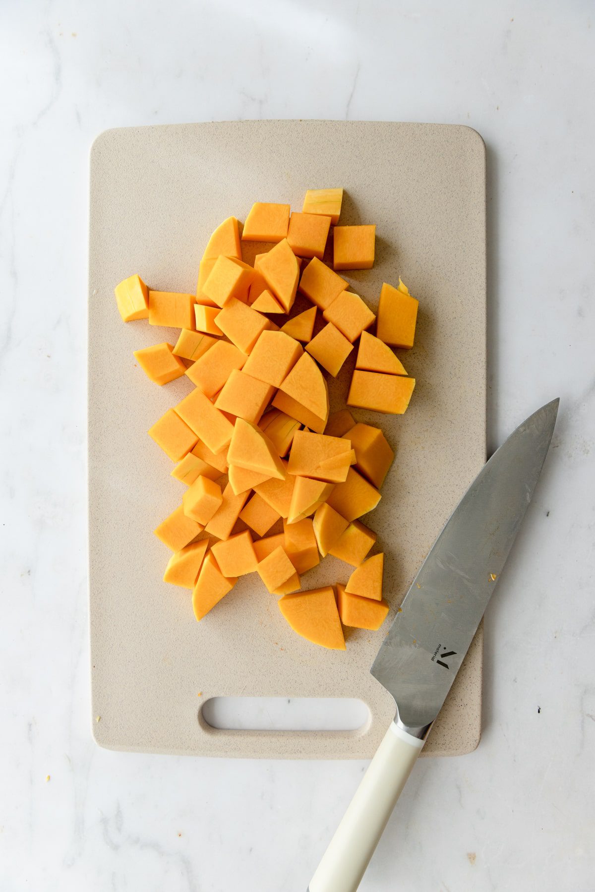 Diced butternut squash on a cutting board next to a knife.
