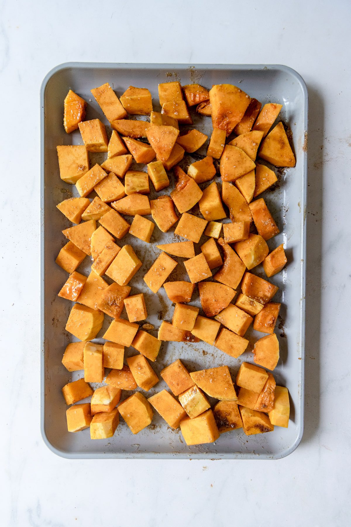 diced butternut squash seasoned with spices on a baking sheet.