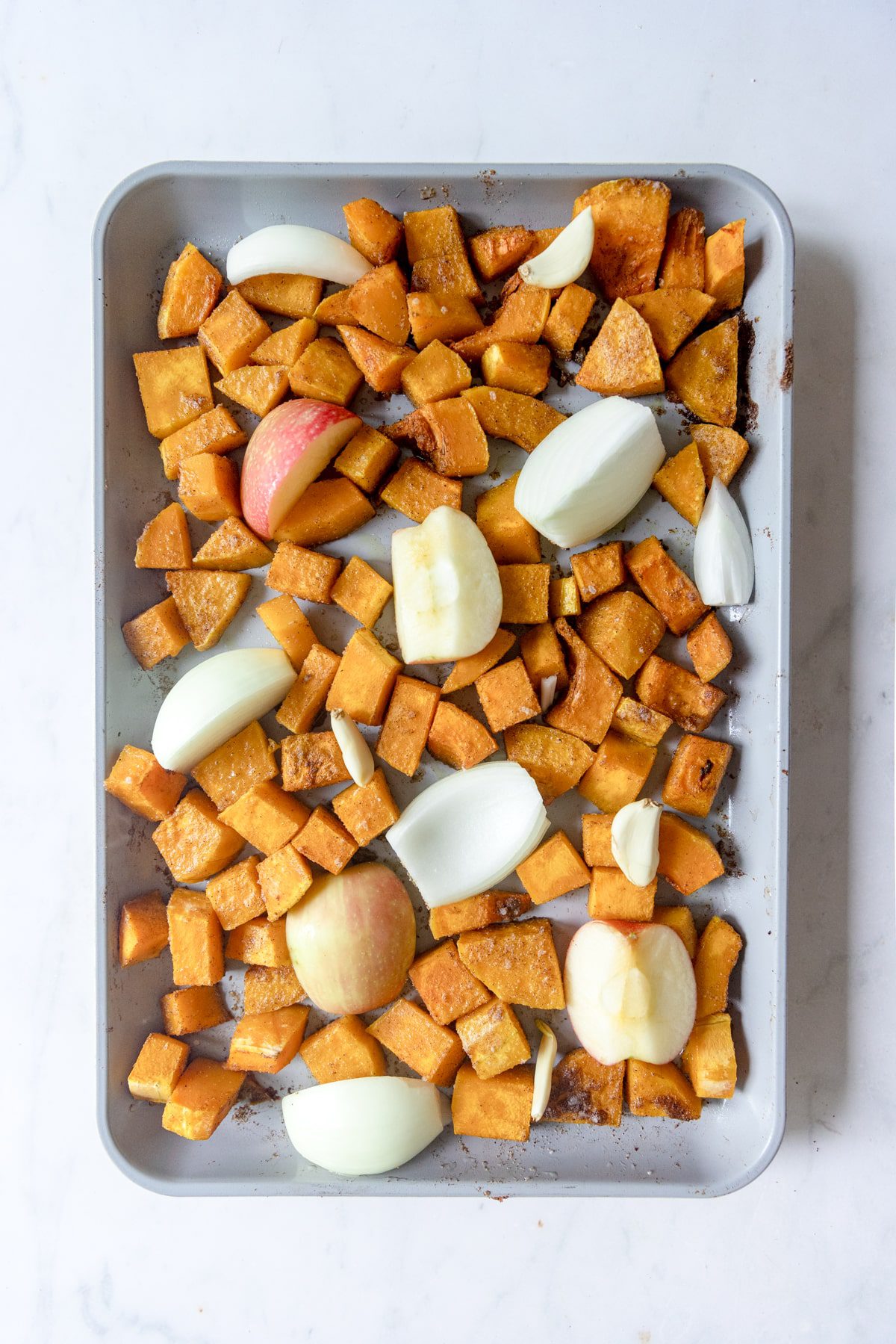 apples, onions, and garlic added to diced roasted butternut squash on a sheet tray.