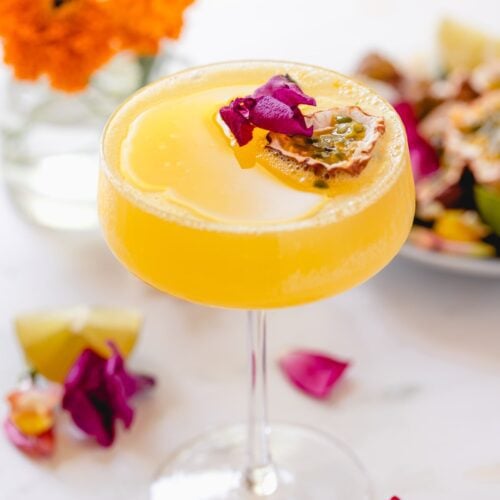 Passion fruit martini in a coupe glass garnished with edible flowers.