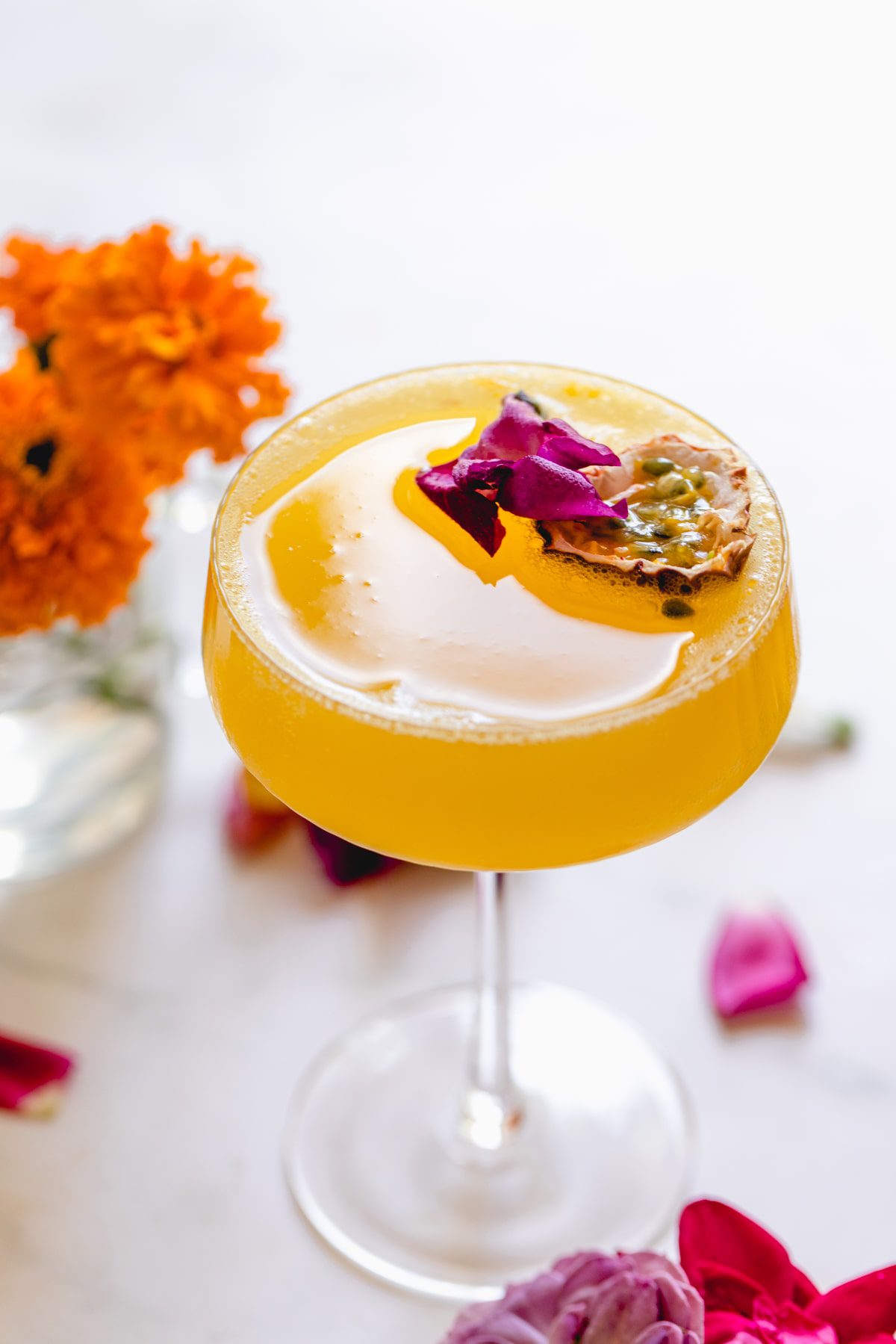 A glass of passion fruit martini with a purple flower as garnish. 