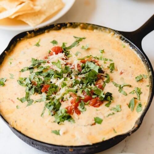 cast iron skillet of smoked queso garnished with tomato and cilantro.