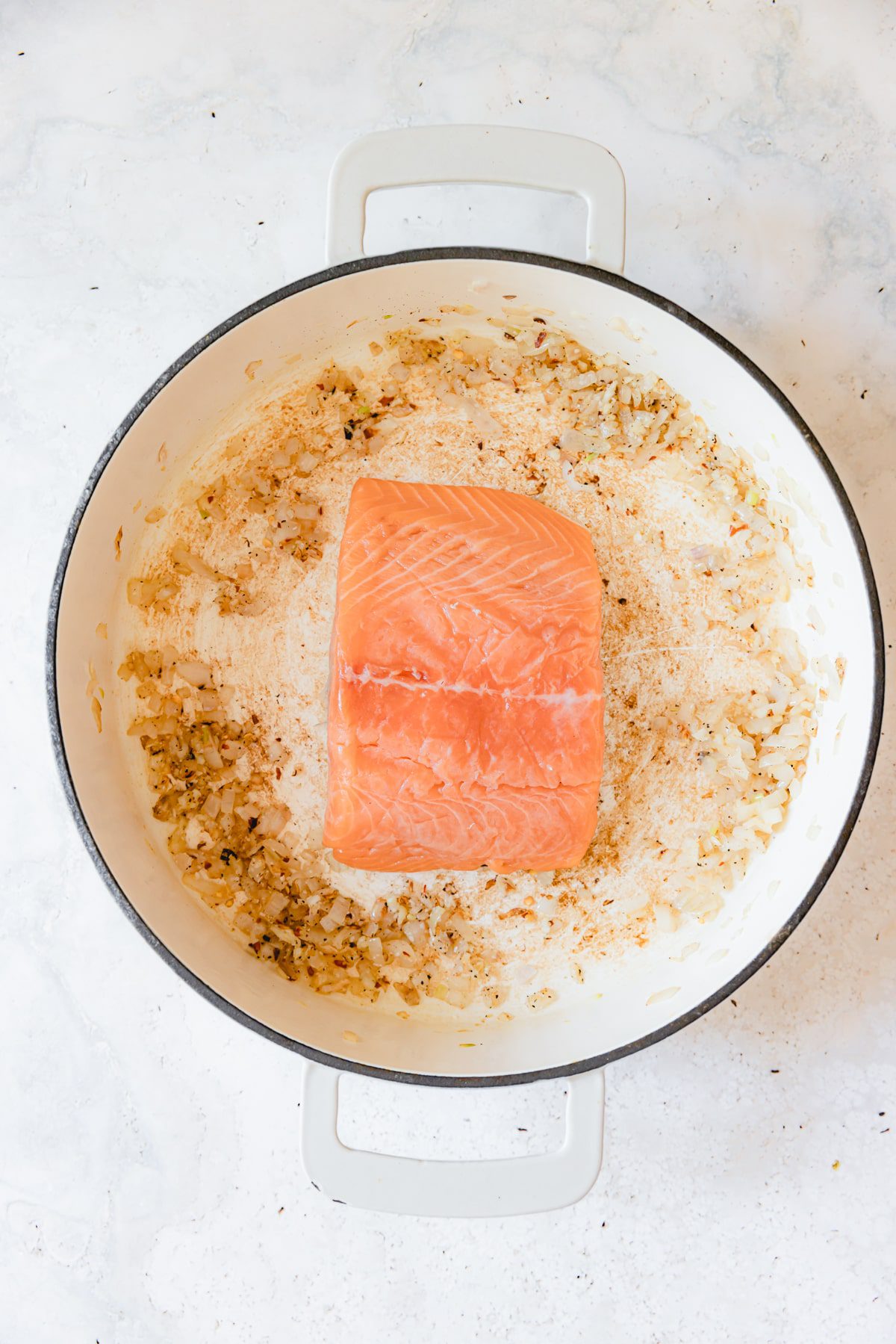 Salmon filet in a skillet with shallot and garlic. 