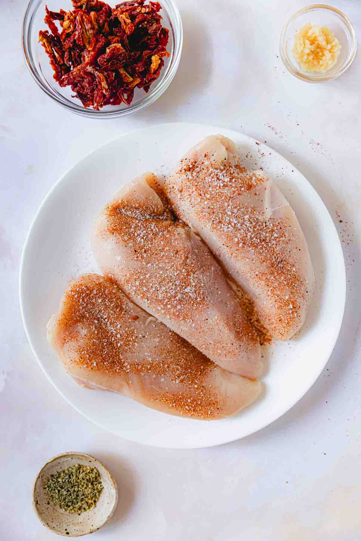 Raw, seasoned chicken on a white plate. 