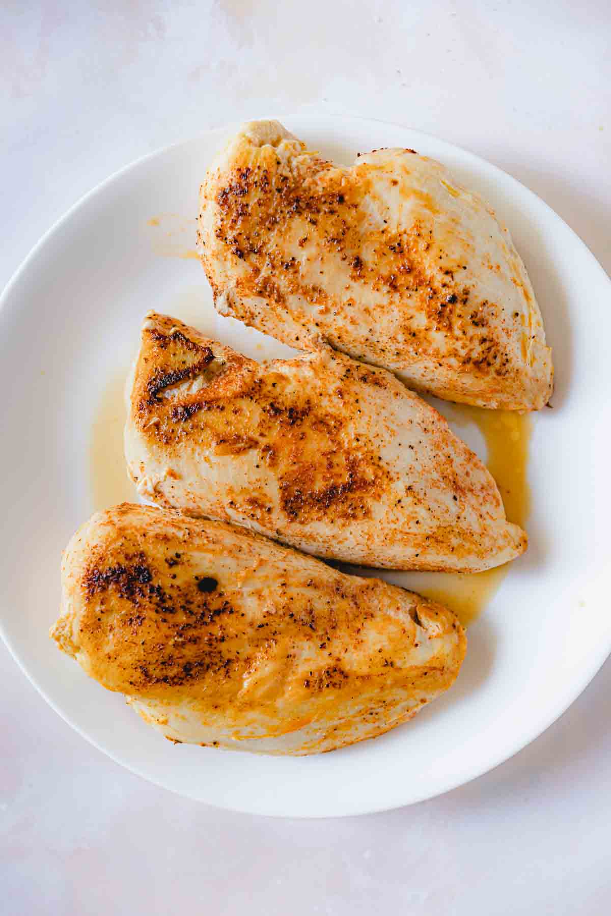 3 cooked chicken breasts set aside on a white plate. 