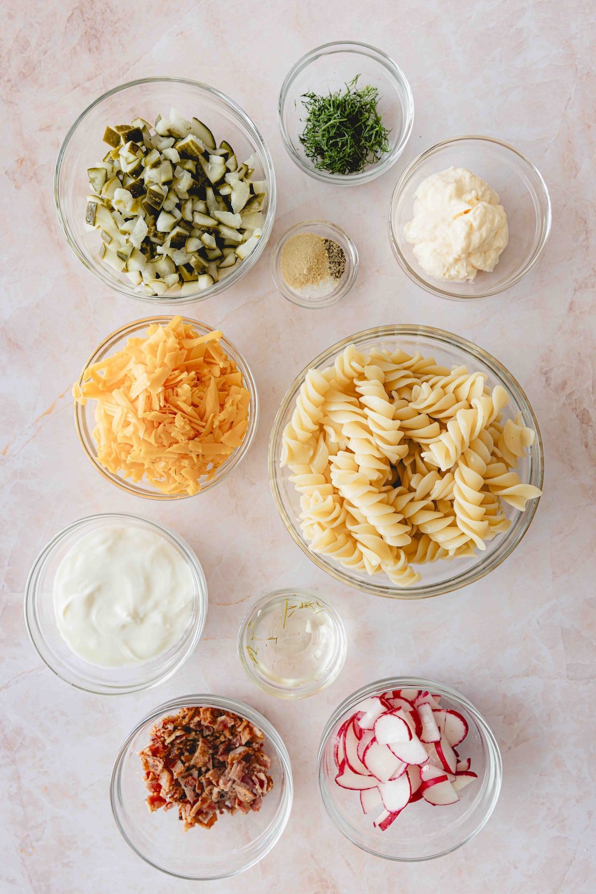 Dill pickle pasta salad ingredients in glass bowls. 