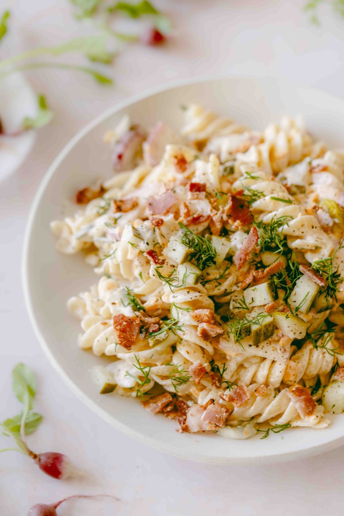 An up-close shot of a white bowl of dill pickle pasta salad with bacon.