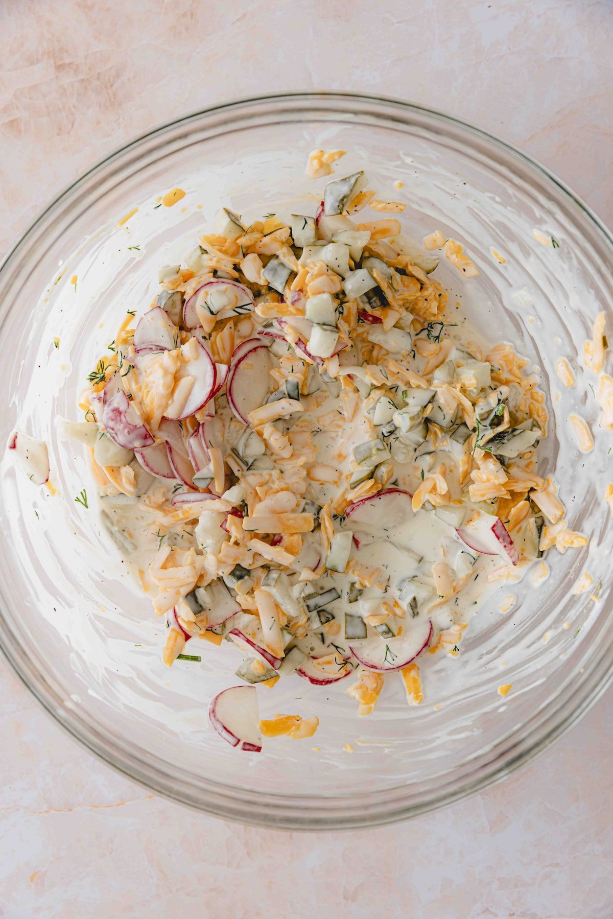 The dill pickle pasta salad toppings tossed with the dressing in a mixing bowl.