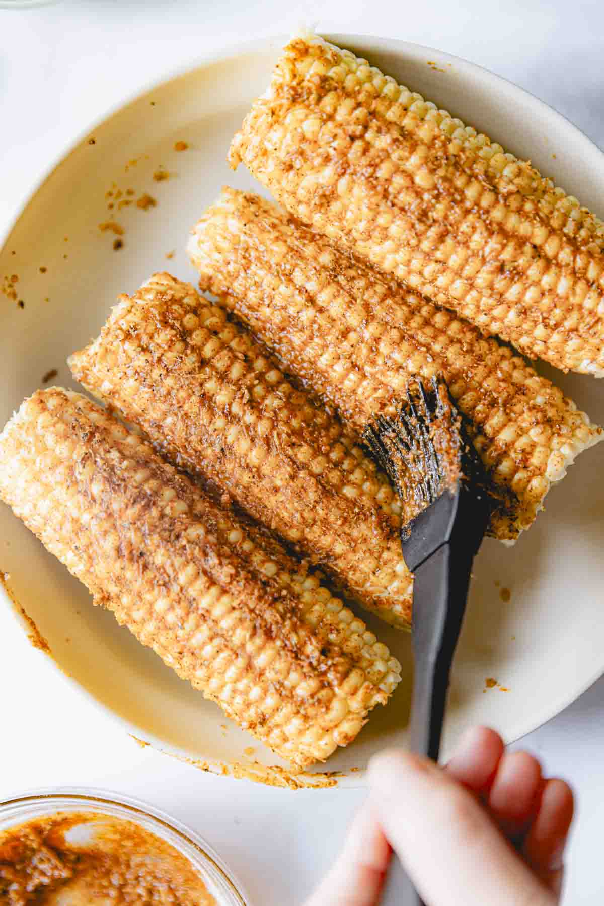 Brushing the butter mixture over uncooked ears of corn. 