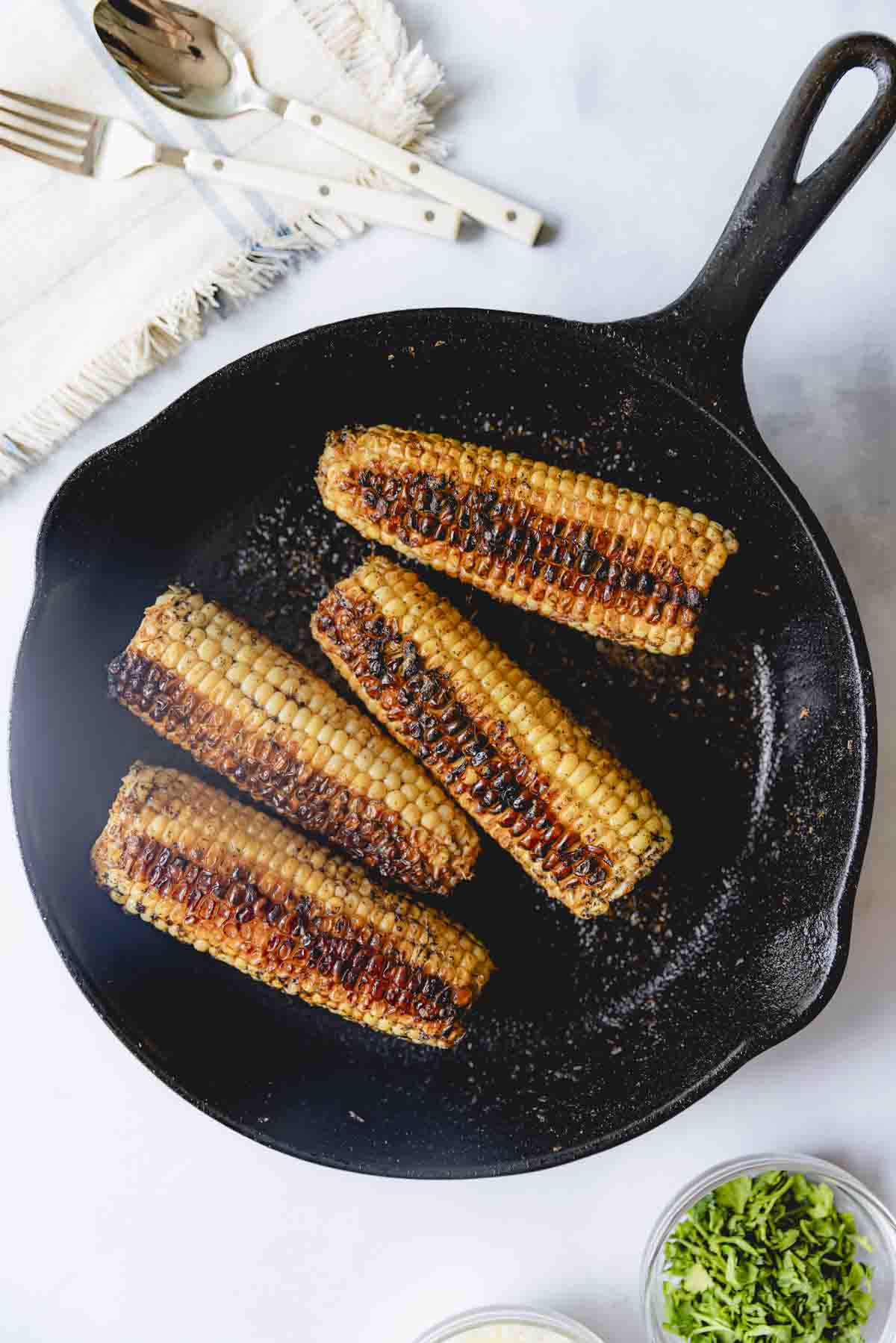 Charred ears of corn in a cast iron skillet. 