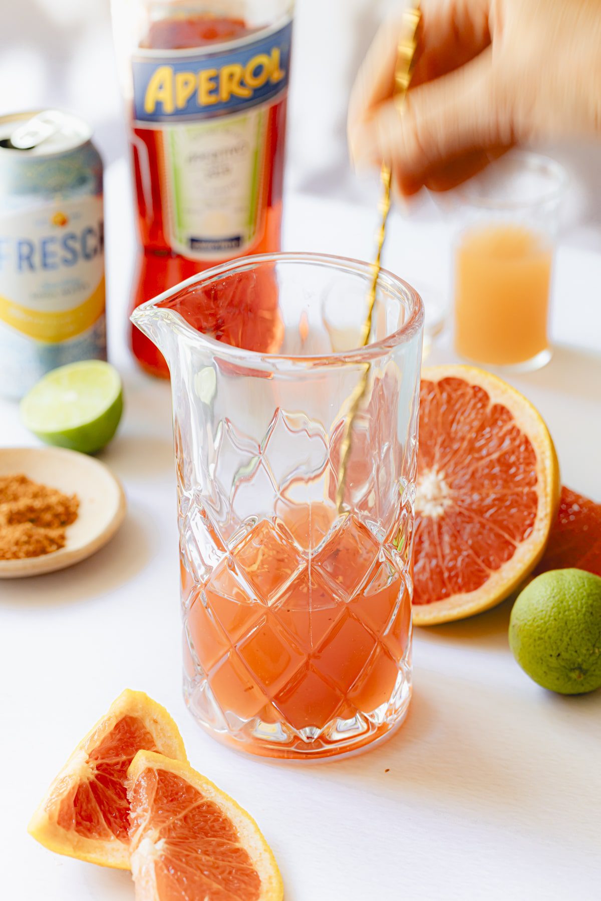 Stirring the Aperol, lime and grapefruit juice, agave, and tequila in a small cocktail pitcher.