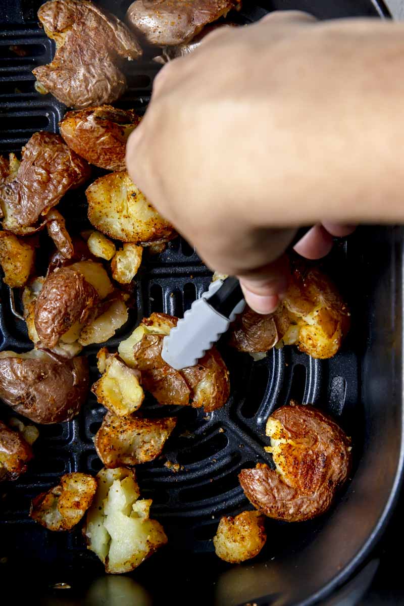 Flipping the red potatoes over in the air fryer halfway through cooking.