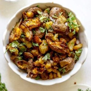 Bowl of crispy red potatoes garnished with green herbs.