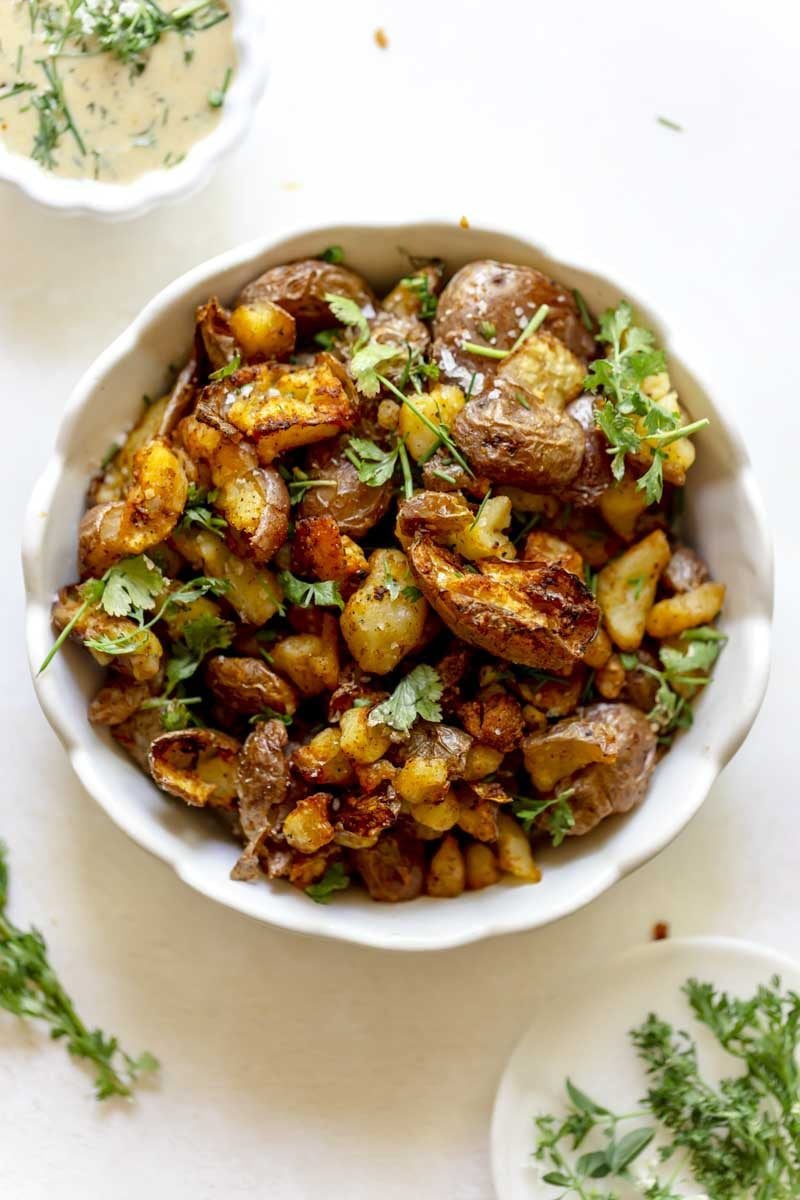 Bowl of crispy red potatoes garnished with green herbs.